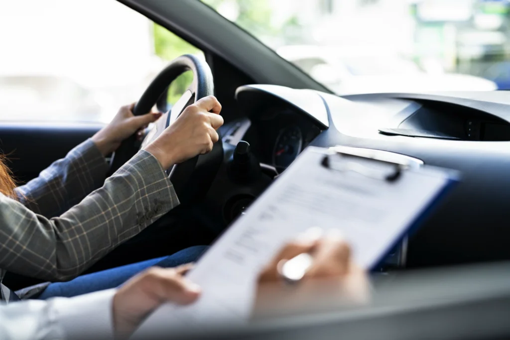 A young woman taking her driver's test with a DMV agent in the passenger seat filling out her evaluation paperwork